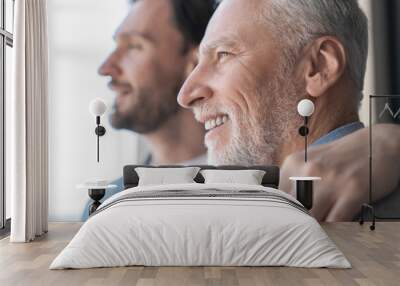 Close up shot of a caucasian young adult son supporting his old elderly senior man looking at the window in future together at home. Happy father`s day! I love you, dad! Wall mural